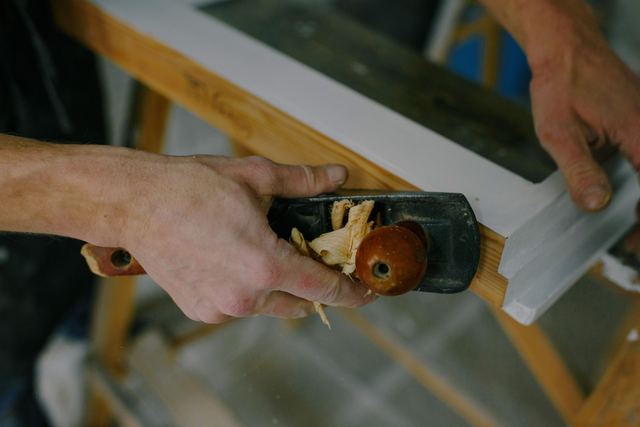 Handen die met een schaaf een wit houten raamkader bijwerken