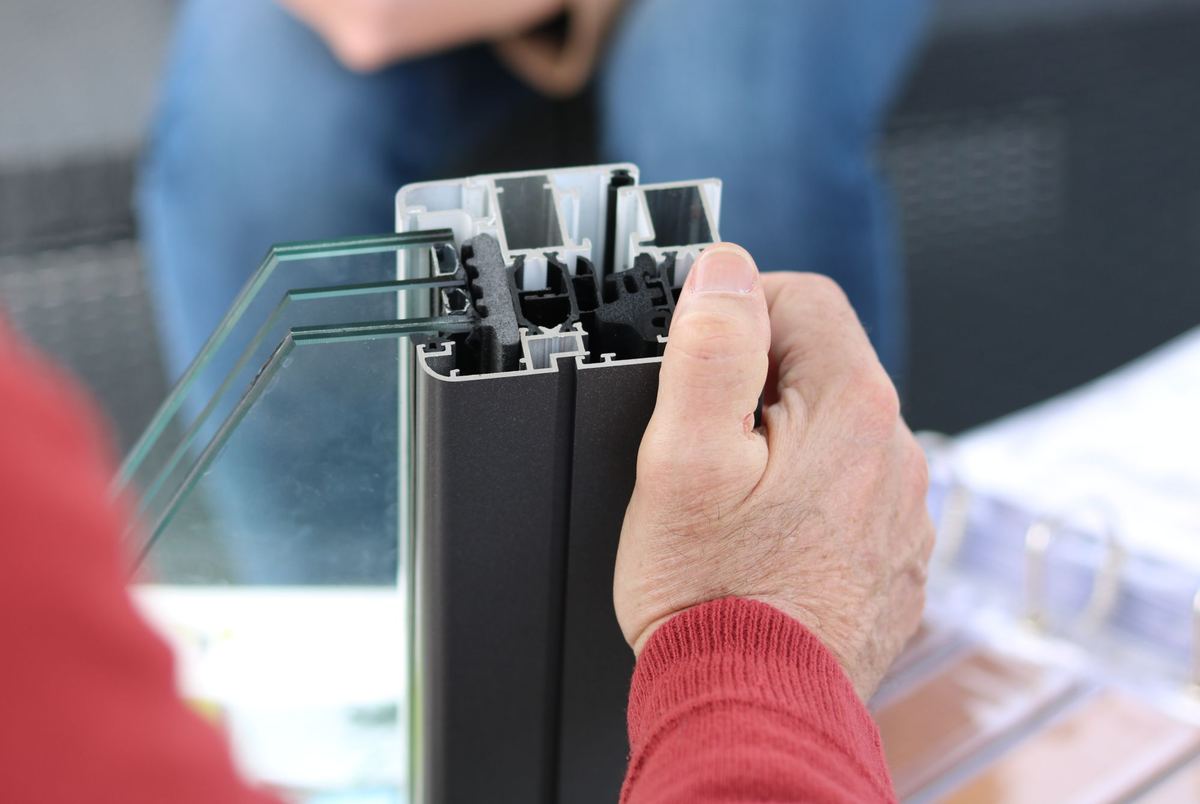 Hand die een doorgezaagd aluminium raamprofiel met drie glasplaten vasthoudt